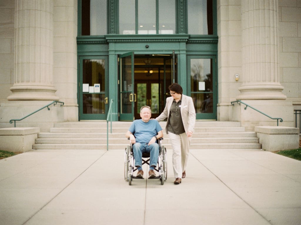 Wheelchair user and companion approaching a broad accessible entrance